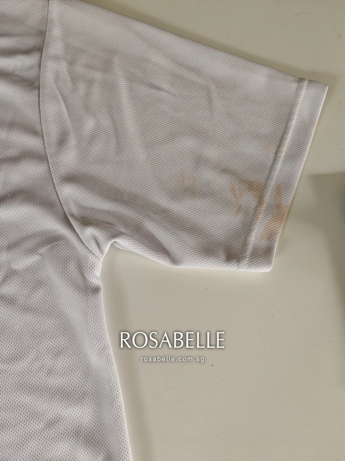 Close view of the T-shirt sleeve and shoulder seam with orange-brown sunscreen blotches on the white knit