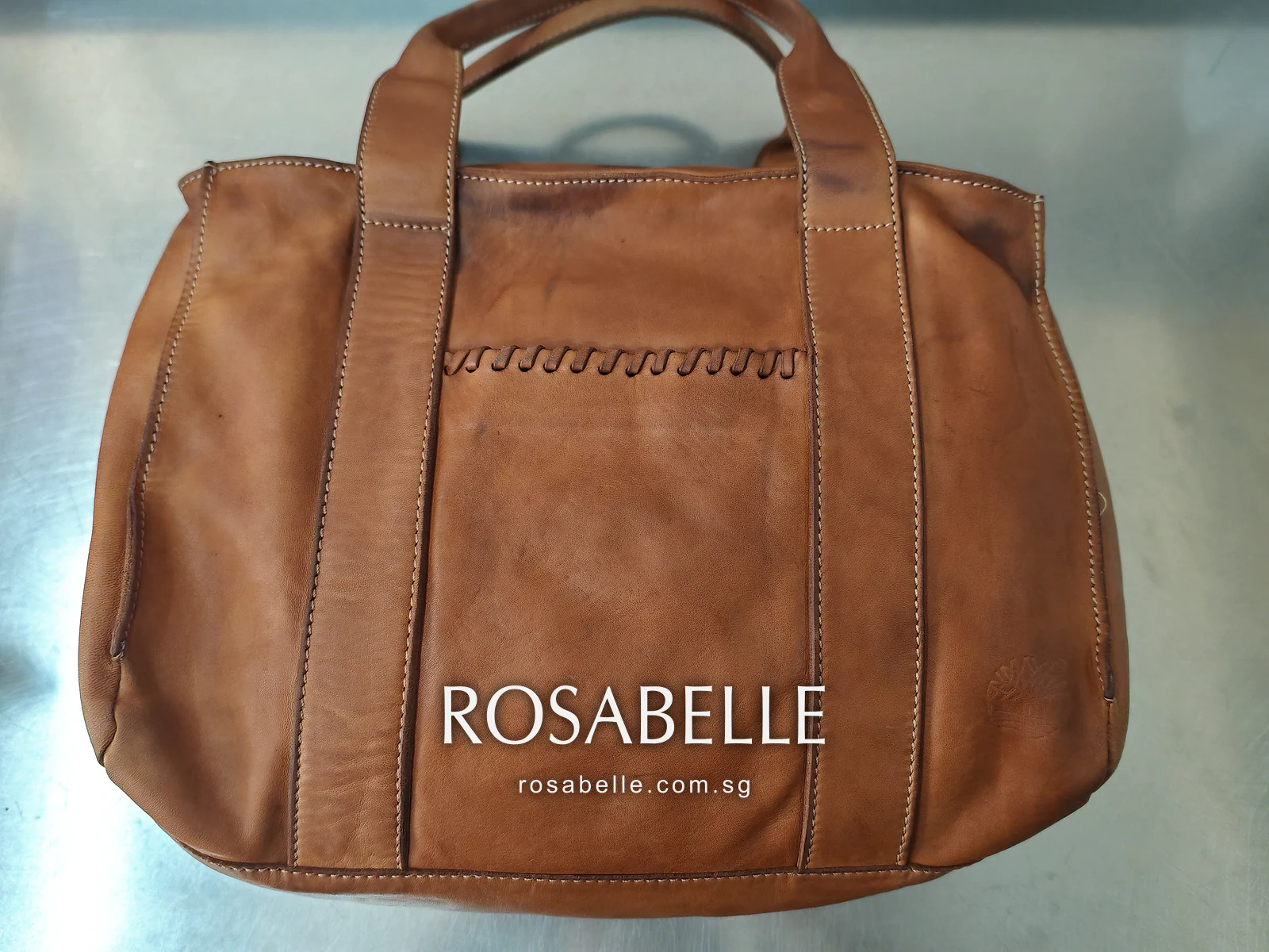 The same tan leather tote front after cleaning, whipstitch detail visible and the tone more even across the panel
