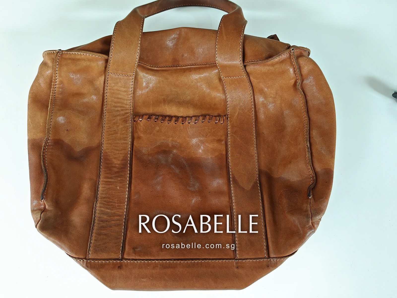 Tan Timberland leather tote darkened by rain, a water line across its lower half, before cleaning